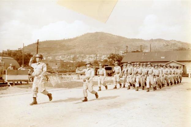 1955年，驻韩美军附编韩军（KATUSA）在列队行进（地点为今天的龙山Camp Conier，照片背景为20世纪50年代的首尔南山 ）