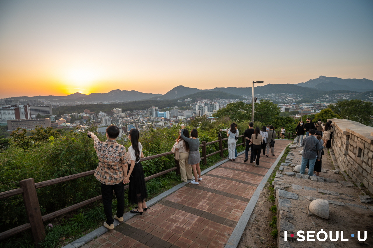 登上骆山公园最高处眺望晚霞映照下的首尔市区的人群